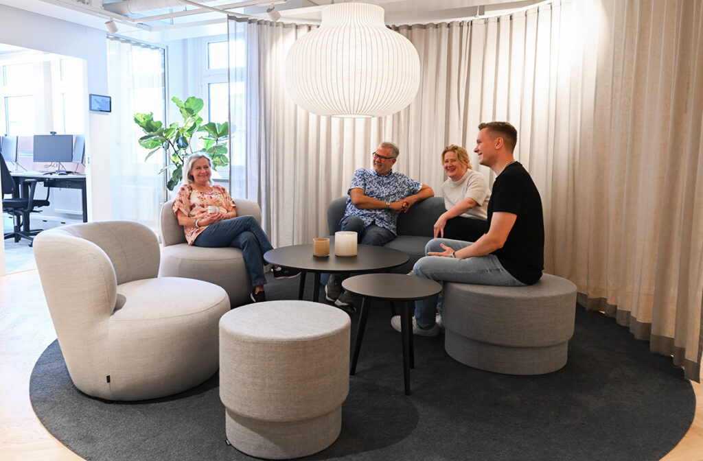 Fyra människor samtalar i lounge. De sitter på sittpuffar och ljuset skapar en mjuk känsla.